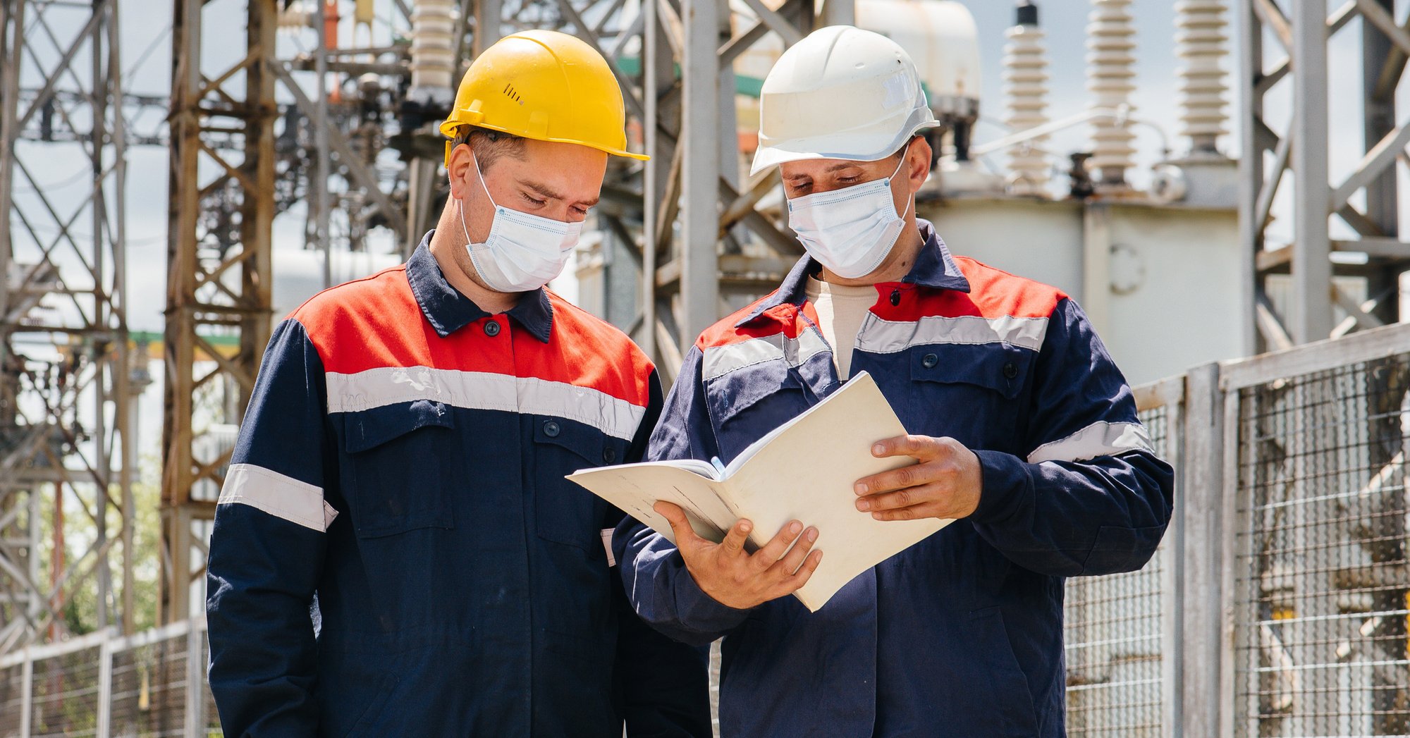 two construction workers wearing paper masks and consulting a guide