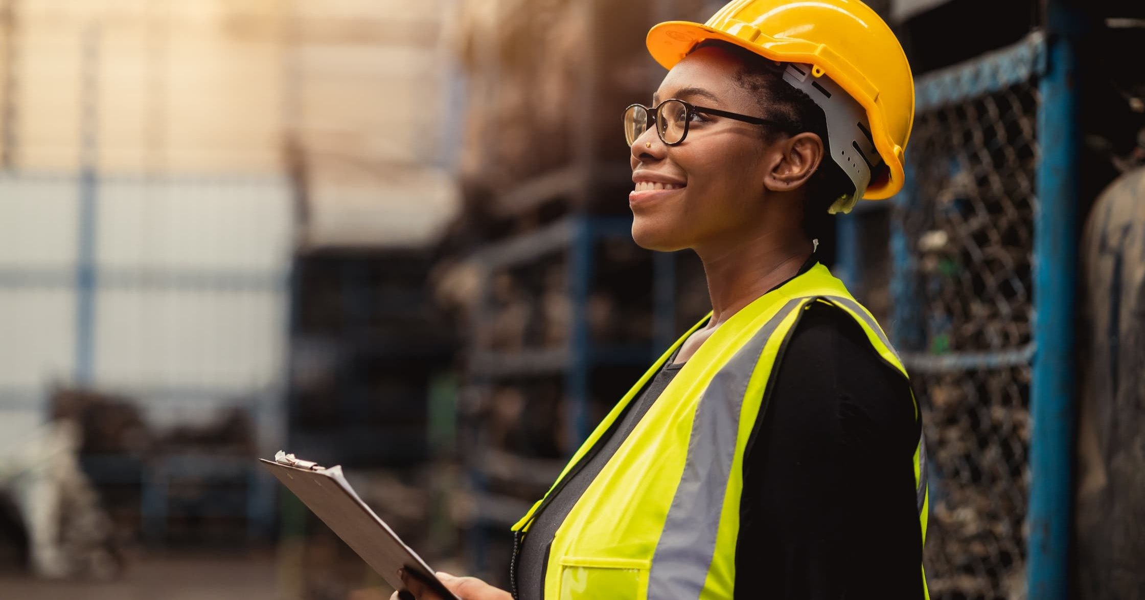 a manufacturing employee holding a clipboard and smiling while doing her job