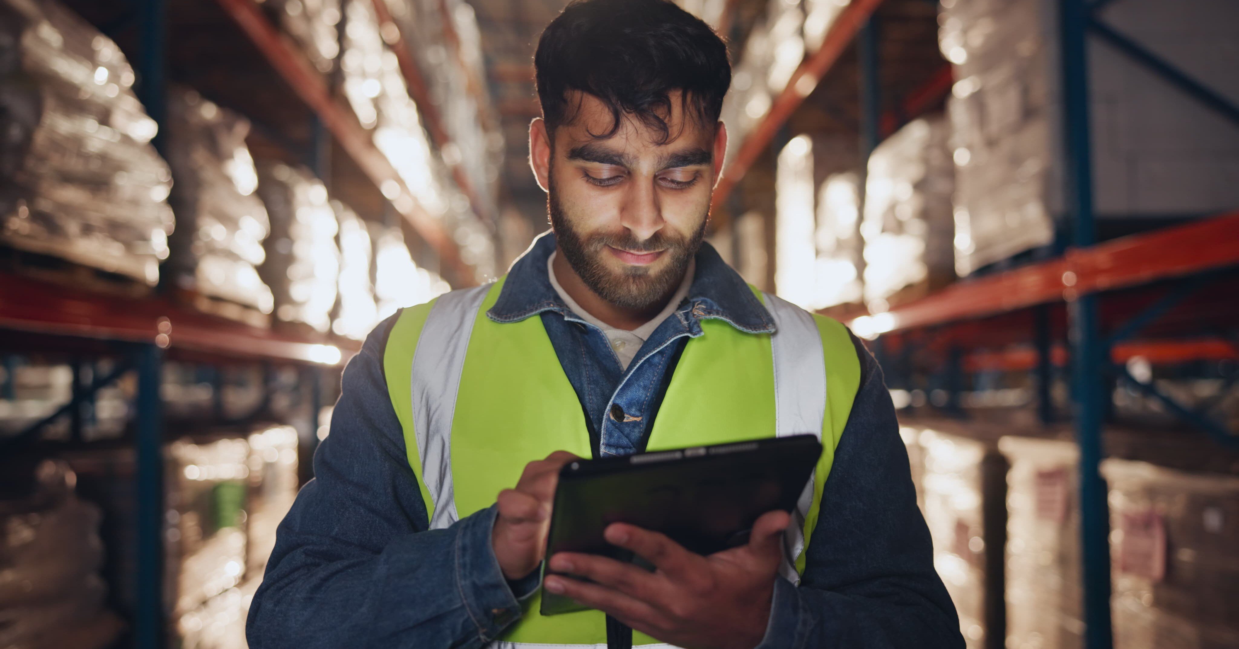 a quality assurance employee wearing a yellow vest and tying on a tablet